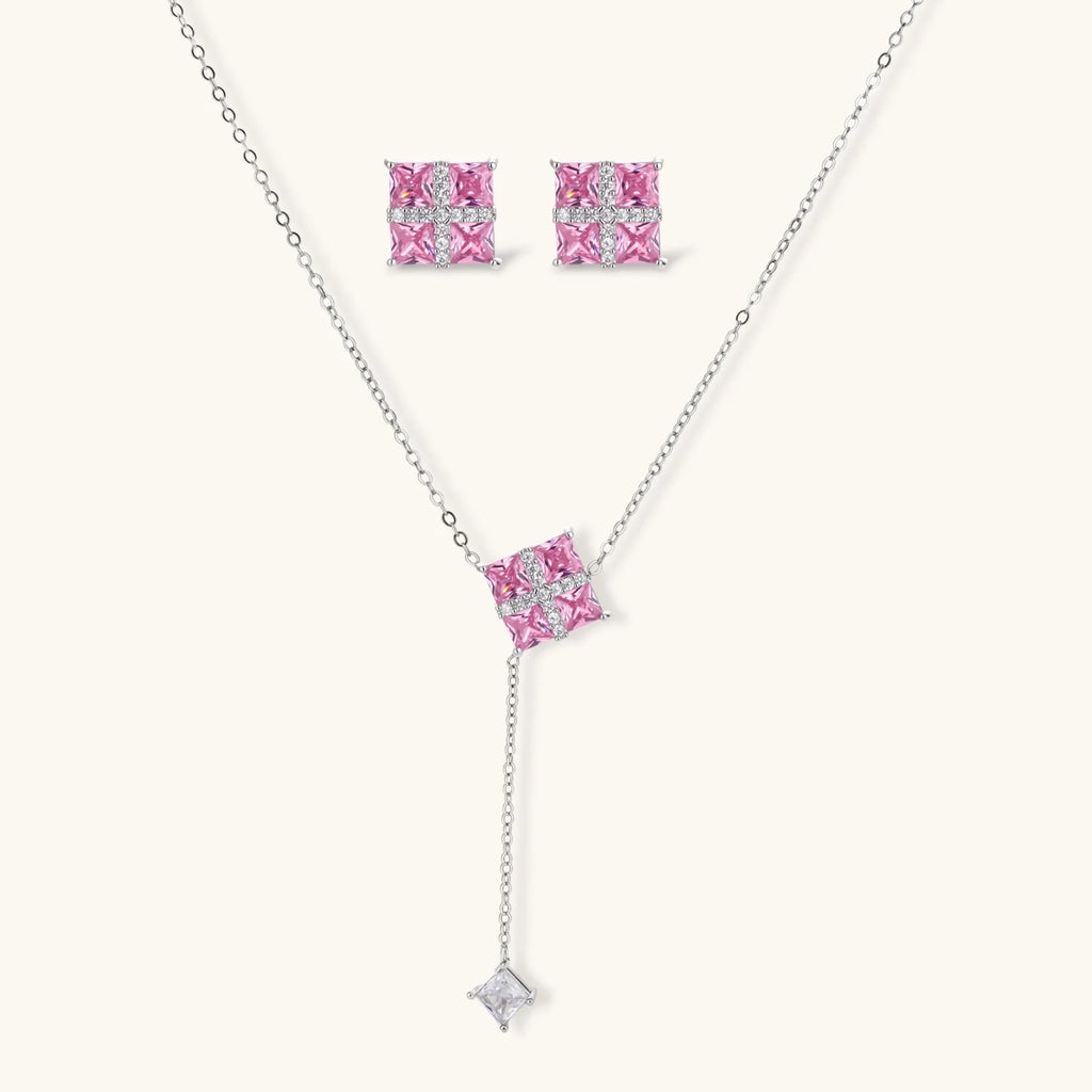 Pink Ribbon Cross set: Y-necklace and square stud earrings with four pink square stones under a white crossed band, front view on a cream background
