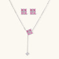 Pink Ribbon Cross set: Y-necklace and square stud earrings with four pink square stones under a white crossed band, front view on a cream background