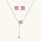 Pink Ribbon Cross set: Y-necklace and square stud earrings with four pink square stones under a white crossed band, front view on a cream background