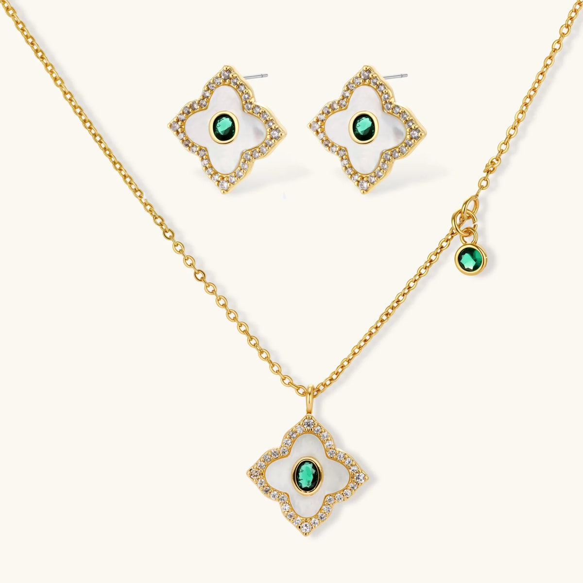 Emerald Bloom set: gold-tone pendant necklace and four-petal stud earrings with white inlay, oval green center stones and clear stone borders, front view